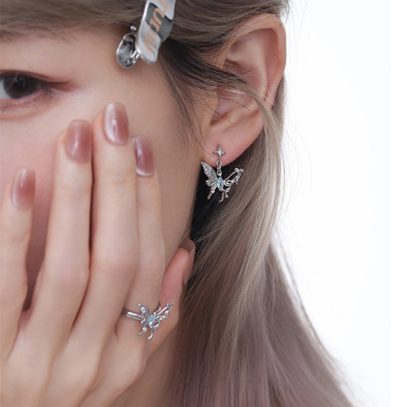Close-up of a silver-tone butterfly drop earring and matching ring with pale blue centre details.
