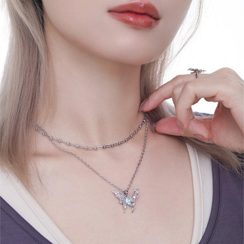 Model wearing layered silver-tone necklaces, including a butterfly pendant with a pale blue centre.