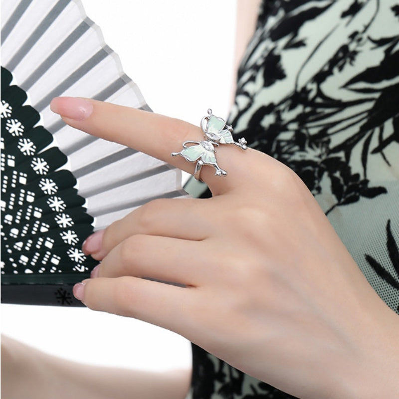Close-up of a silver-tone butterfly ring with pale iridescent wings, worn on a hand holding a folding fan.