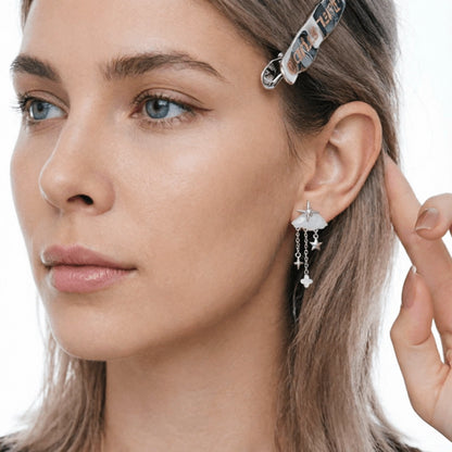 Close-up of a white cloud earring with silver-tone stars and delicate dangling chains, worn by a model.