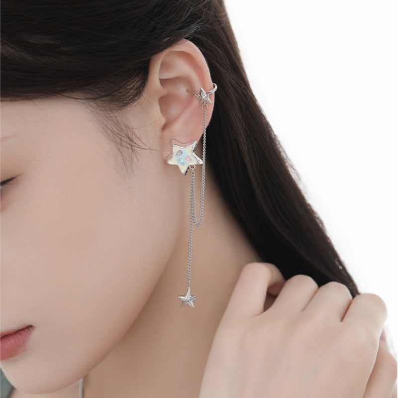 Close-up of a pastel-detailed star earring linked by silver-tone chains to an upper ear cuff, with a dangling small star.