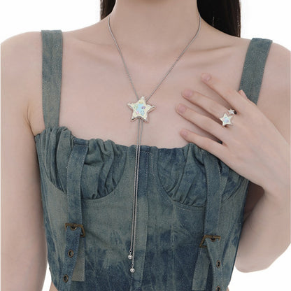 Model wearing a silver-tone star pendant necklace with pastel-coloured details and long chain drops, alongside a matching star ring.