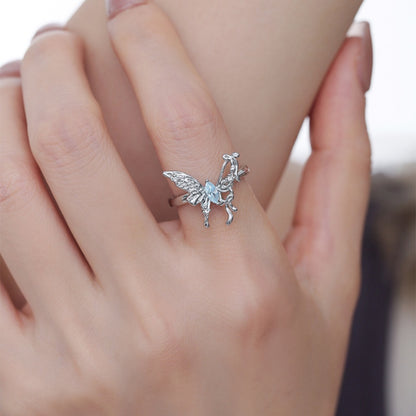 Front close-up of a silver-tone butterfly ring with detailed wings and a pale blue centre, worn on a hand.