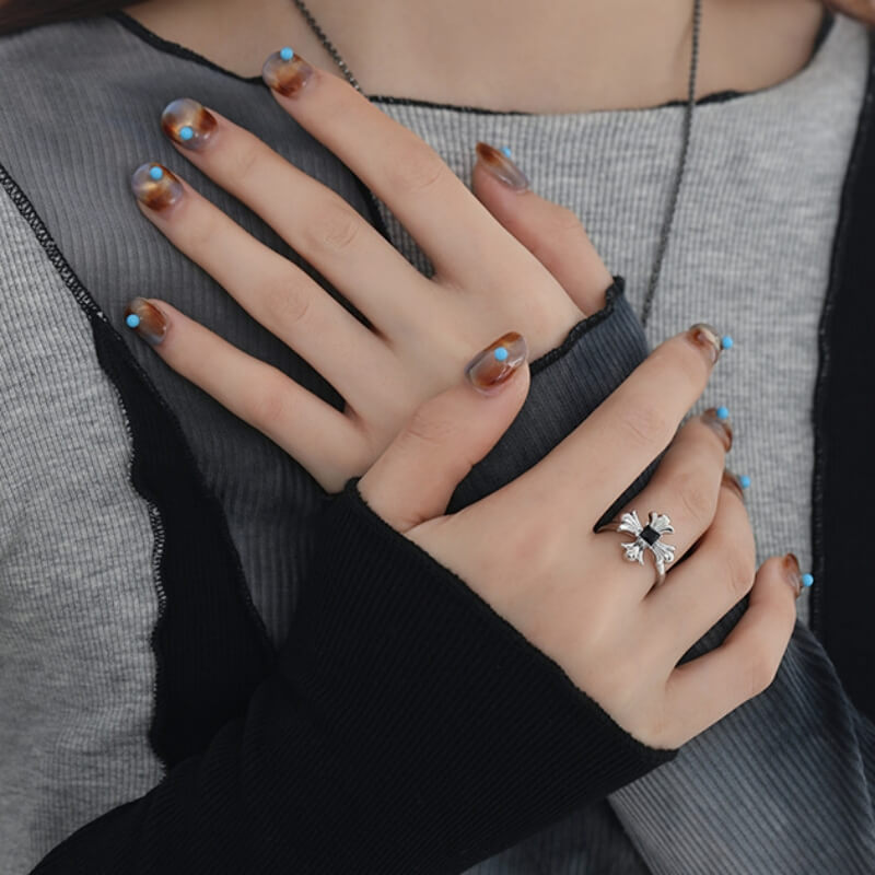 Close-up of a silver-tone gothic cross ring with a black square centre, worn on a model's hand.