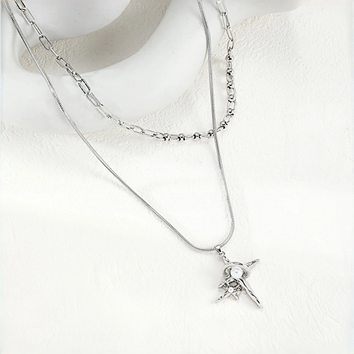 Grunge star cross layered necklace close-up, silver snake chain and paperclip chain layered together with a four-point star and cross pendant featuring pearl accents