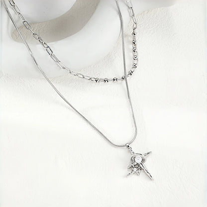 Grunge star cross layered necklace close-up, silver snake chain and paperclip chain layered together with a four-point star and cross pendant featuring pearl accents
