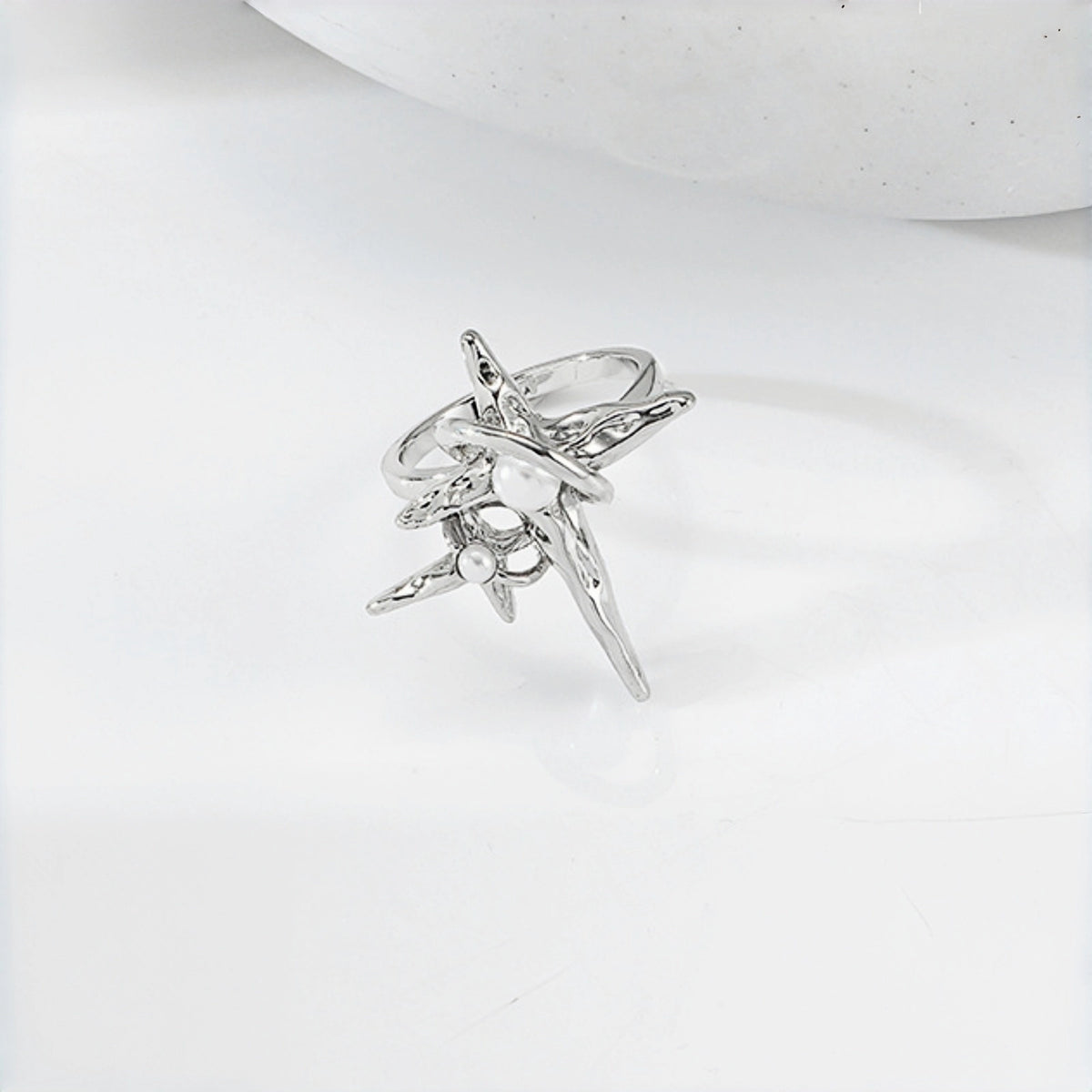 Grunge star cross ring close-up, open silver band with an asymmetric four-point star and cross charm featuring a pearl accent
