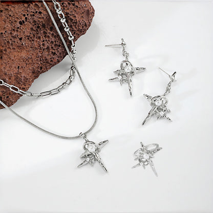 Grunge star cross jewellery set flat lay, layered necklace, drop earrings and ring all featuring silver star and cross charms with pearl accents, beside a textured rock
