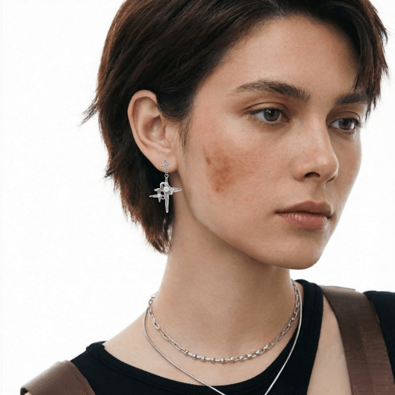 Close-up of a silver-tone star-cross drop earring with long pointed arms, worn by a model.
