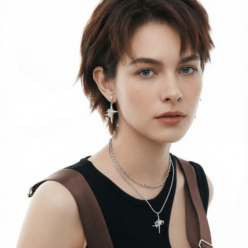 Front view of a model wearing silver-tone star-cross drop earrings and a matching pendant on layered chains.