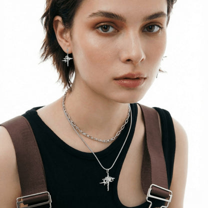 Model wearing layered silver-tone necklaces with a star-cross pendant and matching drop earrings.
