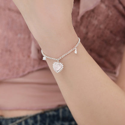 Close-up of a silver-tone chain bracelet with a textured heart charm and smaller dangling charms on a wrist.
