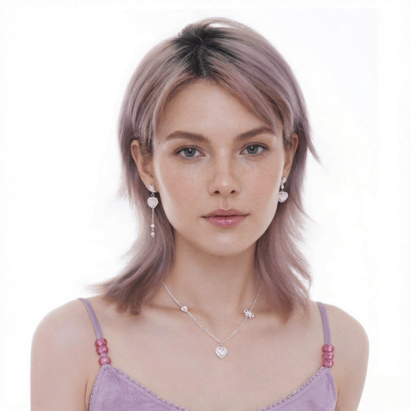Model wearing a silver-tone heart pendant necklace and mismatched heart earrings, one with a long chain drop.