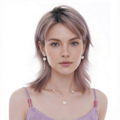 Model wearing a silver-tone heart pendant necklace and mismatched heart earrings, one with a long chain drop.