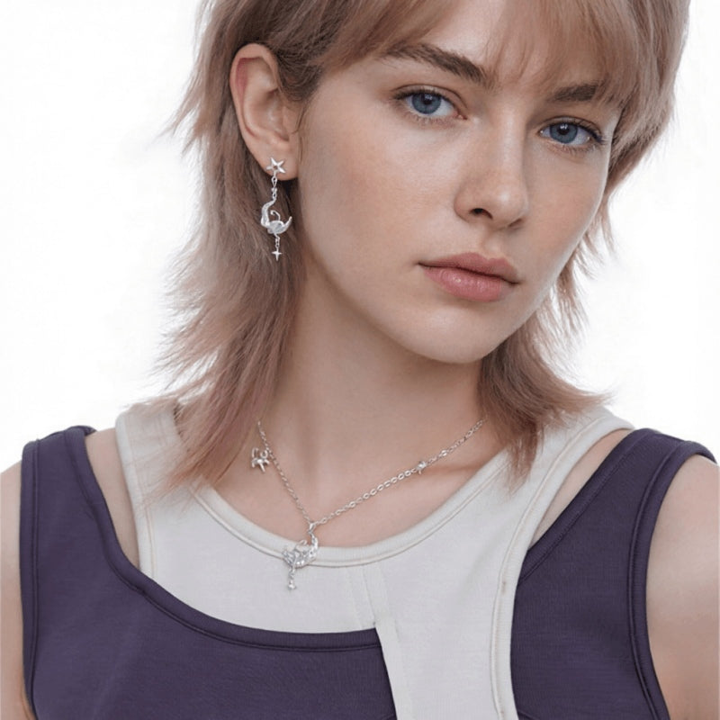 Model wearing a silver-tone cat-and-crescent-moon drop earring and matching necklace with star details.