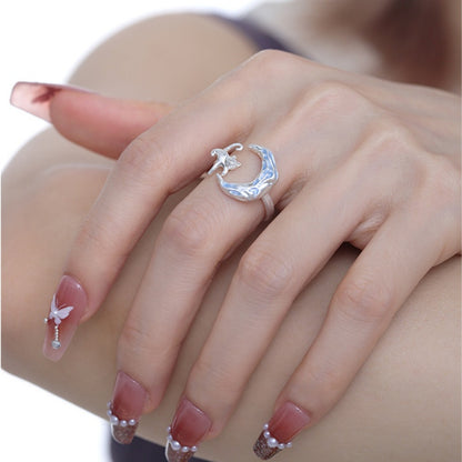 Close-up of a silver-tone crescent moon ring with a small cat figure, worn on a hand.