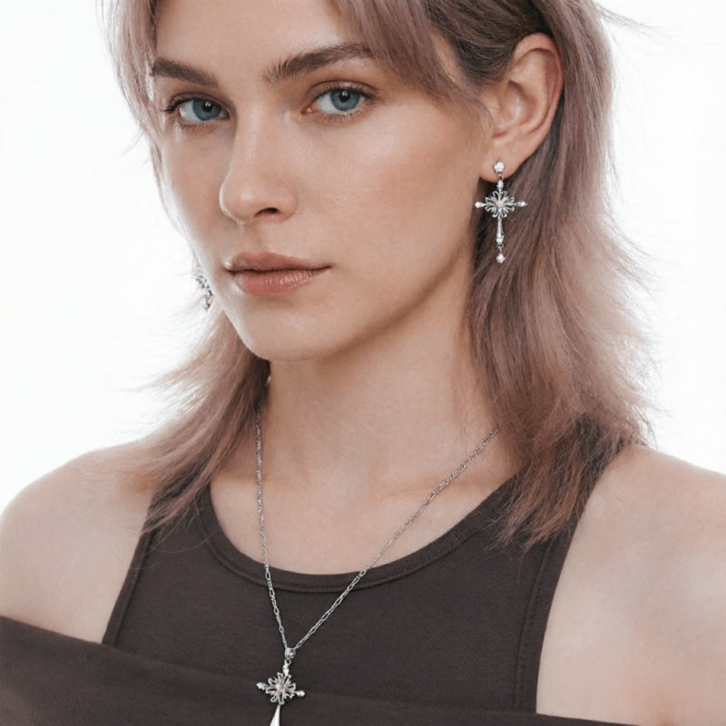 Close-up of a model wearing a silver-tone cross drop earring and matching cross pendant necklace.