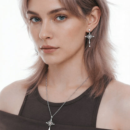 Close-up of a model wearing a silver-tone cross drop earring and matching cross pendant necklace.