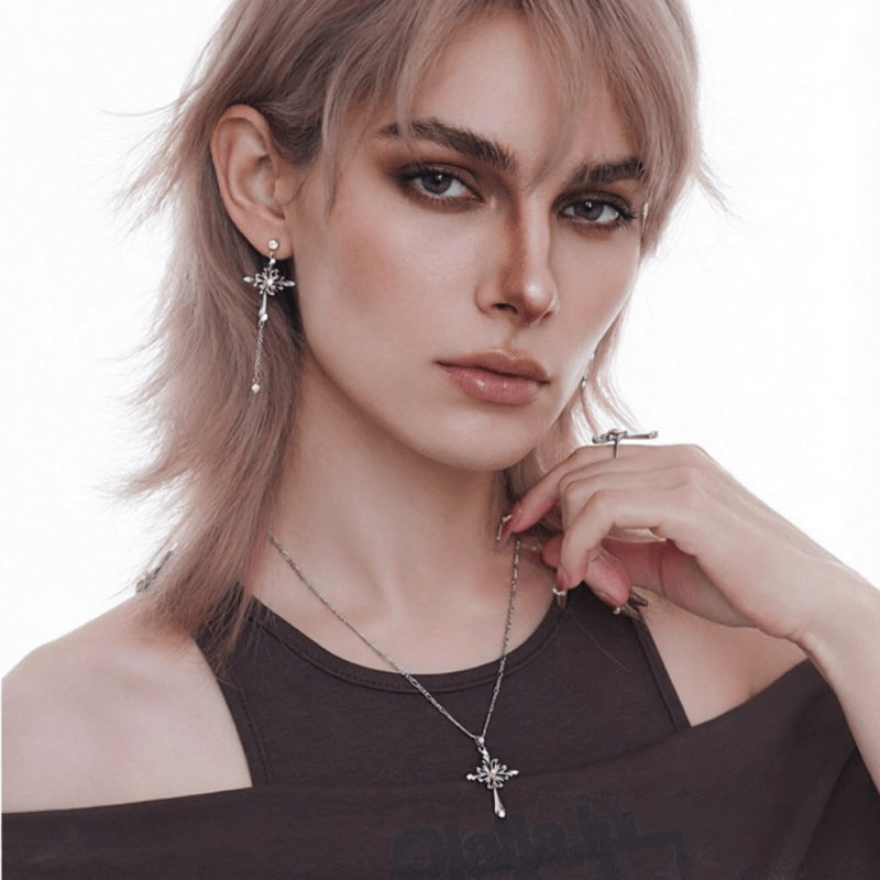 Model wearing a silver-tone ornate cross necklace and a long drop earring with a matching cross design.