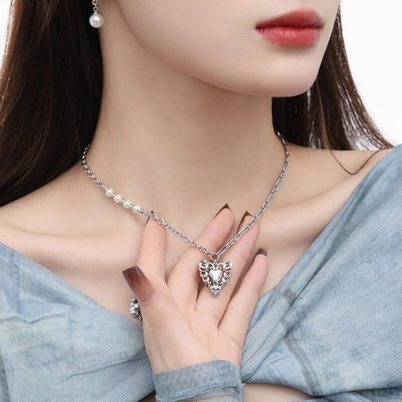Model wearing an ornate silver-tone heart pendant necklace with pearl-like beads along one side of the chain.