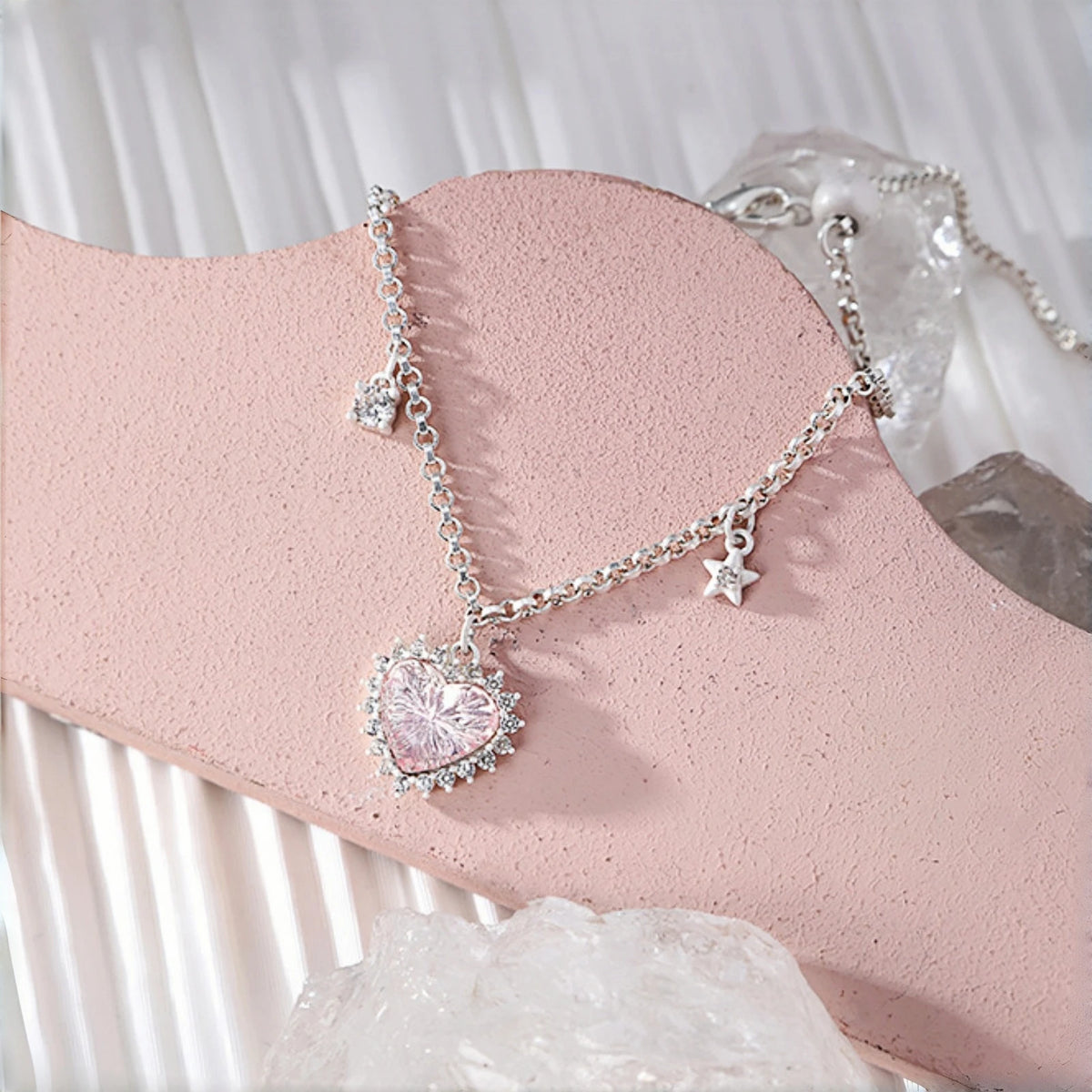 Pink heart princess bracelet close-up, pink crystal heart charm with clear crystal halo on a chain with dangling clear heart and star charms, on a pink display stand