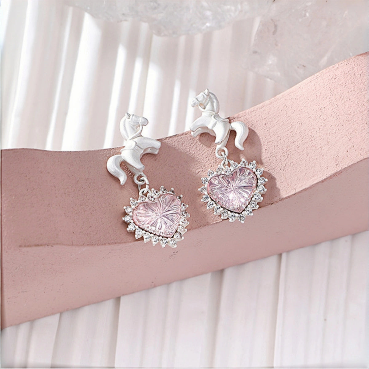 Pink heart princess earrings close-up, pair of pink crystal heart drops with clear crystal halos, topped with white enamel unicorn studs
