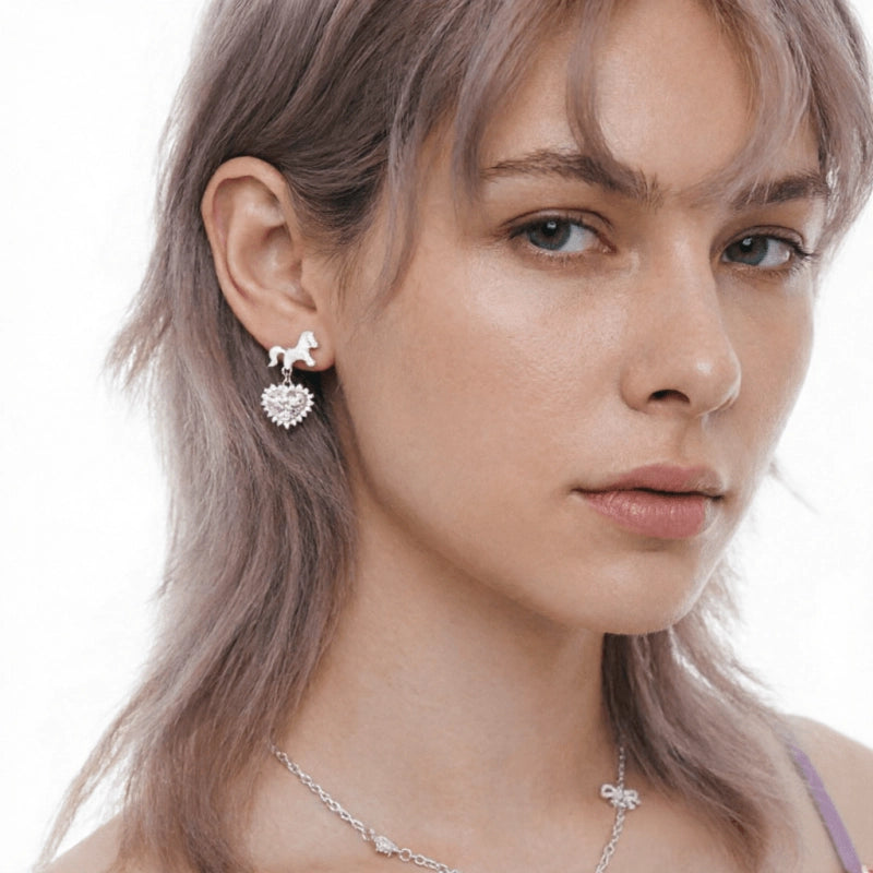 Close-up of a model wearing a silver-tone unicorn earring with a dangling pale pink heart charm.
