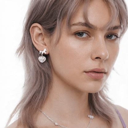 Close-up of a model wearing a silver-tone unicorn earring with a dangling pale pink heart charm.