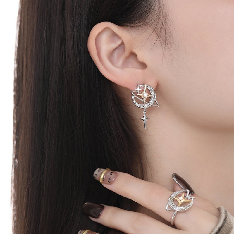 Close-up of a silver-tone planet earring with a dangling star charm, worn with a matching ring.
