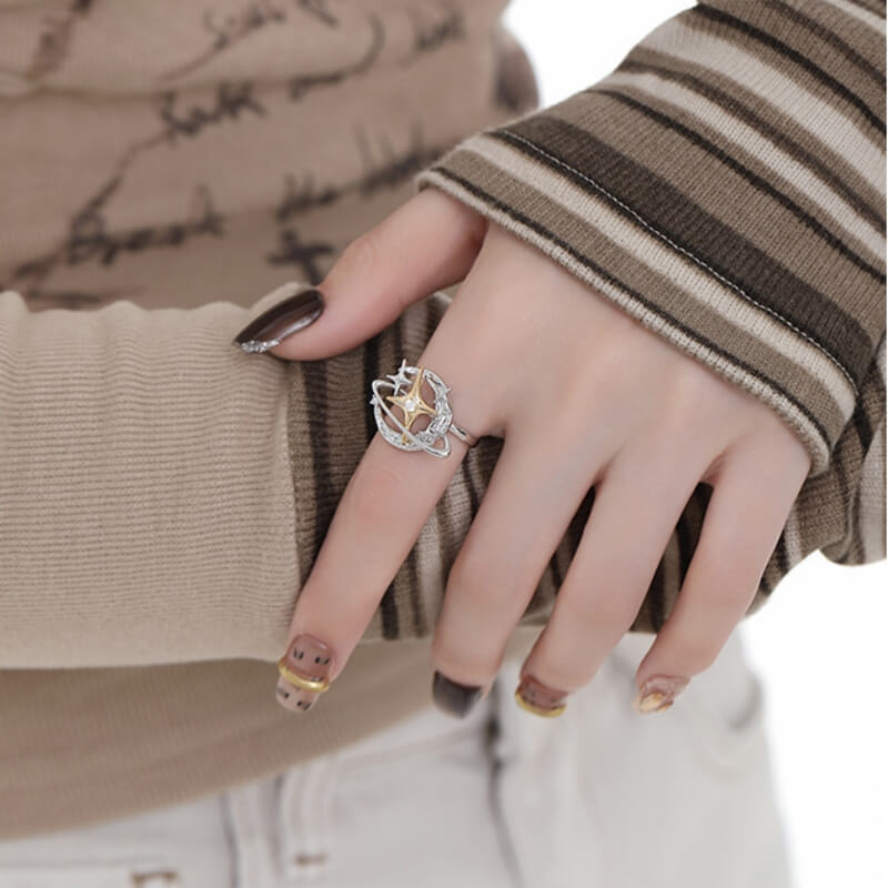 Close-up of a silver-tone orbital ring with a gold-tone star centre, worn on a model's hand.