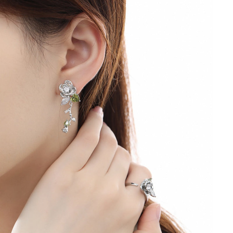 Model wearing a silver-tone rose drop earring with green leaf details and a matching rose ring.