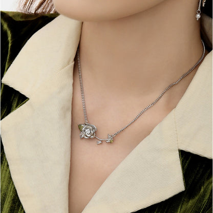 Close-up of a silver-tone rose necklace with green leaf details and a small dangling charm.