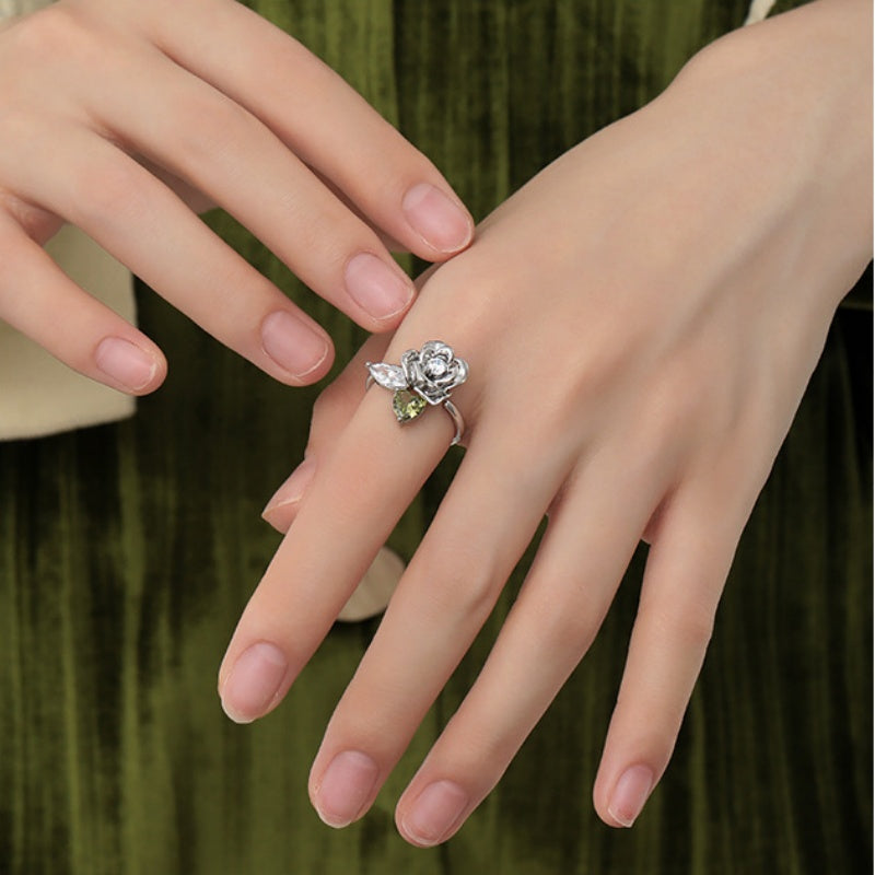 Close-up of a silver-tone rose ring with leaf details worn on a model's hand.