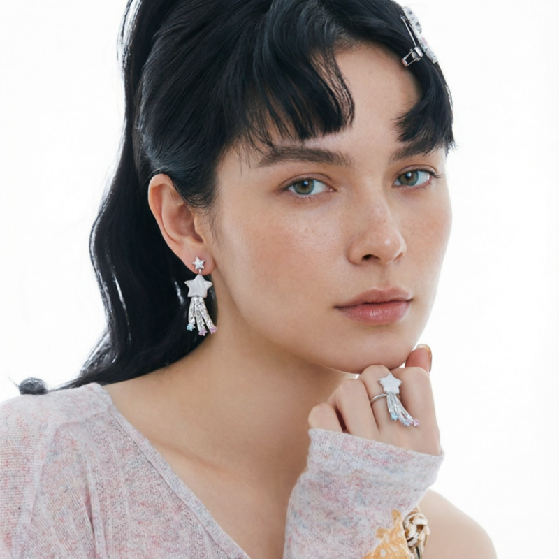 Model wearing a white star drop earring with trailing details and a matching star ring.