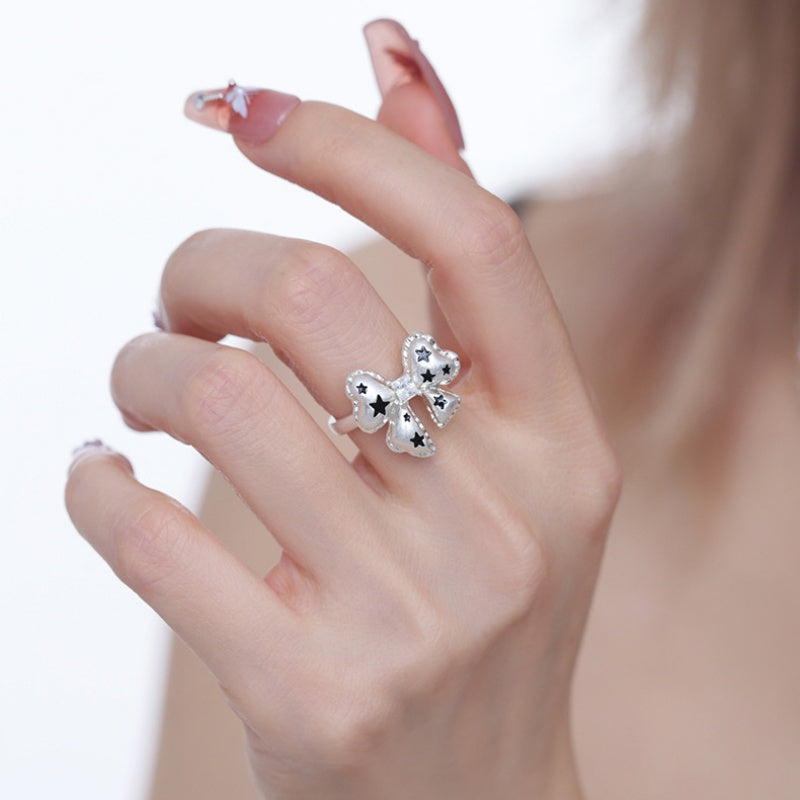 Close-up of a white bow ring with black star details in a silver-tone setting, worn on a hand.