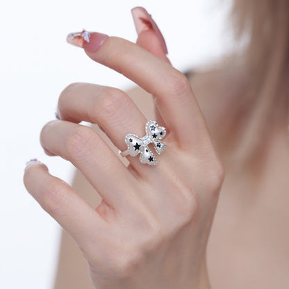 Close-up of a white bow ring with black star details in a silver-tone setting, worn on a hand.