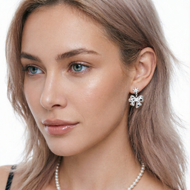Close-up of a white bow drop earring with small black star details, worn by a model.