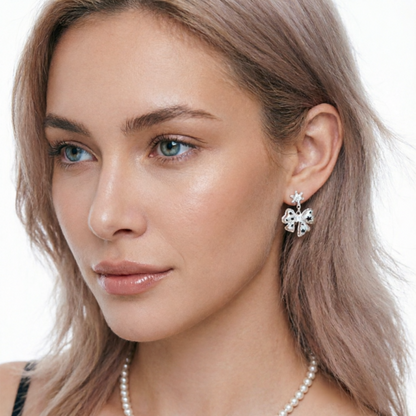 Close-up of a white bow drop earring with small black star details, worn by a model.