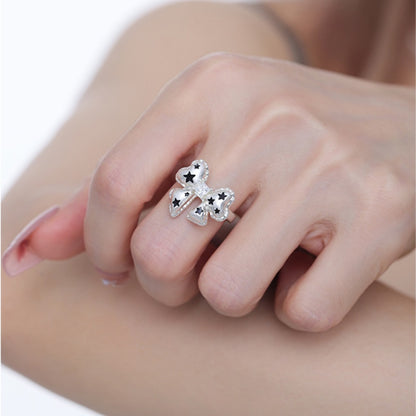 Close-up of a white bow ring with black star details, worn on a hand.
