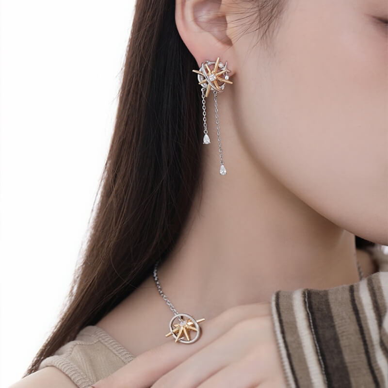 Close-up of a two-tone starburst earring with two dangling chains, worn with a matching pendant necklace.