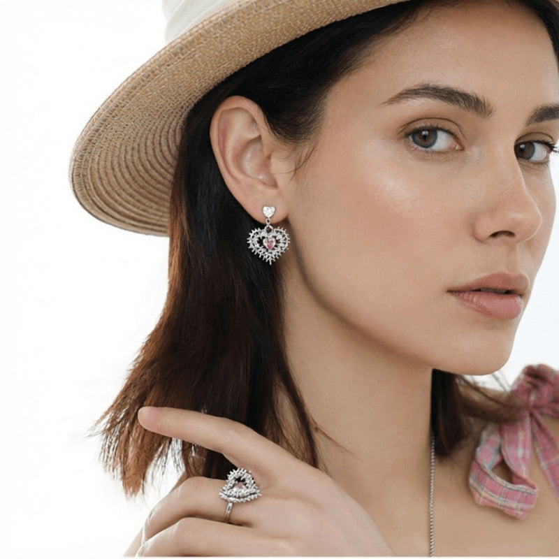 Model in a straw hat wearing a silver-tone thorn-framed heart earring and matching ring with pale pink centres.