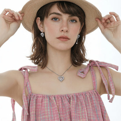 Front view of a model wearing a thorn-framed heart necklace and mismatched heart earrings, one with a long chain drop.
