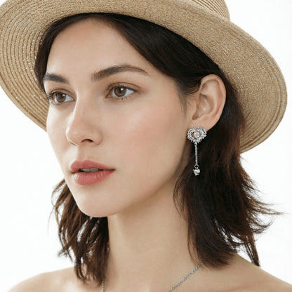 Model wearing a silver-tone thorn-framed heart earring with a pale pink centre and a long dangling chain.