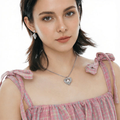 Model wearing a silver-tone thorn-framed heart necklace and matching drop earring with pale pink centres.