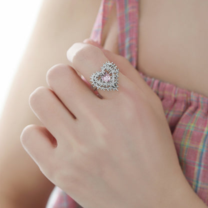 Close-up of a silver-tone thorn-framed heart ring with a pale pink centre, worn on a hand.