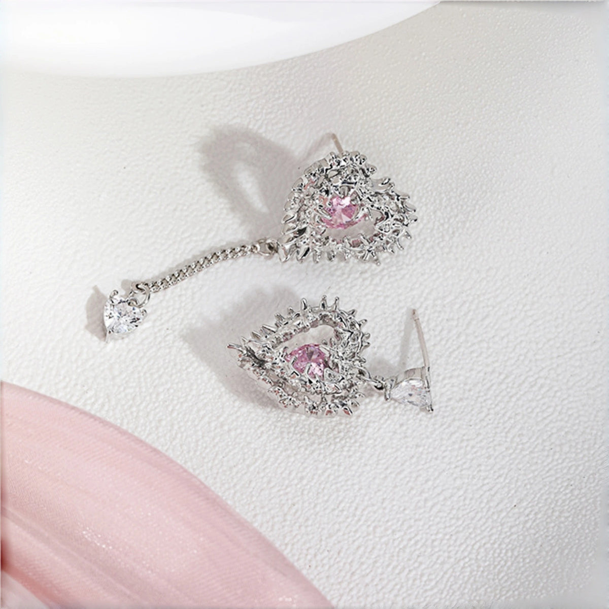 Thorned pink heart earrings close-up, pair of silver thorn-framed heart earrings with pink crystal stones and a mismatched dangling charm