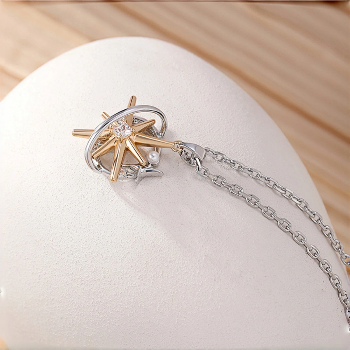 Two-tone starburst pendant necklace close-up, gold starburst charm with a silver ring frame and clear crystal centre, small silver star and pearl accent, on a rolo chain