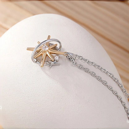 Two-tone starburst pendant necklace close-up, gold starburst charm with a silver ring frame and clear crystal centre, small silver star and pearl accent, on a rolo chain