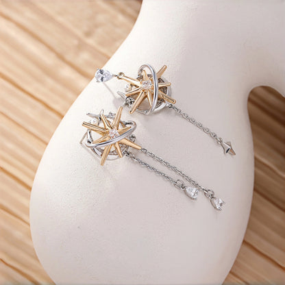 Two-tone starburst drop earrings close-up, pair of gold starburst studs with silver ring frames and clear crystal centres, each with a dangling chain and crystal charms