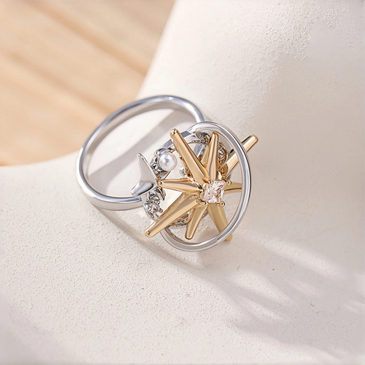 Two-tone starburst ring close-up, open silver band with a gold starburst charm featuring a clear crystal centre, small silver star and pearl accent